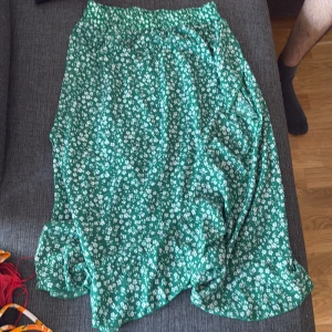 Grön blommig omlottkjol från ONLY - Grön omlottkjol från ONLY i storlek M med vitt blommönster och volangkant. Kjolen har en elastisk midja och är perfekt för vår och sommar. Lätt och flowy känsla som ger en chill vibe till outfiten.