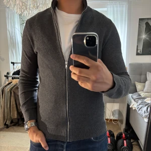 Mörkgrå kofta från Jack & Jones XS - Snygg mörkgrå kofta från Jack & Jones i storlek XS. Tröjan har hel dragkedja framtill, ribbade muddar och krage. Materialet är stickat och känns mjukt och bekvämt. Perfekt för lager-på-lager och passar till jeans eller chinos.