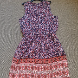 Blommig klänning från GAP - Superfin ärmlös kortklänning från GAP med blommigt mönster i marinblått, rött och vitt. Klänningen har knytband i midjan och dekorativ kant nertill med orientaliskt inspirerat mönster. Perfekt för sommarens alla tillfällen!