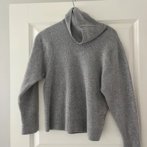 Grå polotröja från Wera i ullmix - Mysig grå polotröja från Wera med hög krage och lång ärm. Tröjan är stickad i en mjuk ullblandning och har ribbade muddar vid ärmslut och nederkant. Storlek S men är liten i storleken