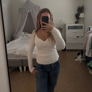 Vit ribbad långärmad tröja med v-ringning - Supersnygg vit ribbad tröja från H&M med v-ringad hals och lång ärm. Figurnära passform. Perfekt att styla med jeans eller kjol för en clean look. Mjuk och stretchig. Använt fåtal gånger 