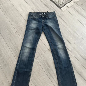 Blå jeans från Gang Jeans med brodyr - Snygga blå jeans från Gang Jeans med klassisk tvätt och cool broderad detalj i färg på bakfickorna. Modellen har raka ben och normal passform, perfekt till sneakers eller boots. Jeansen har fem fickor och bälteshällor. Bootcut jeans lågmidjade.