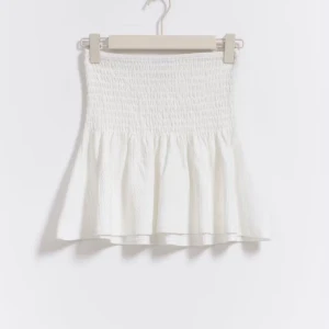 Vit kortkjol från Gina Tricot  - Supersöt vit kortkjol från Gina Tricot i storlek XS. Kjolen har smockad midja och lätt volang nedtill, vilket ger en luftig och somrig känsla. Perfekt för varma dagar och enkel att matcha med crop tops eller linnen. Man kan även använda denna tröjan som en topp. Den är aldrig använd och köptes för 279kr. 
