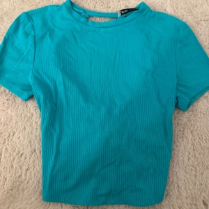 Turkos ribbad topp med snörning i ryggen  - Säljer en turkos ribbad topp från new yorker i storlek XS. Toppen har korta ärmar, croppad passform och snygg snörning i ryggen som ger en cool detalj. Materialet är stretchigt och väldigt bekvämt. 