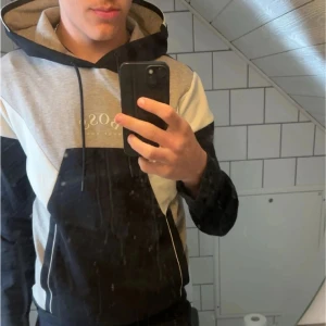 Grå och svart hoodie från Hugo Boss - Säljer en snygg beige och svart hoodie från Hugo Boss med vita detaljer. Hoodien har en klassisk design med justerbar huva och logotyp framtill. Perfekt för en stilren och bekväm look.stick 10/10 stilren🫡
