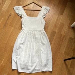 Vit kortklänning med volangärmar - Superfin vit kortklänning med volangärmar och broderade prickar. Endast använd en gång men säljer då den tyvärr inte passar mig längre.