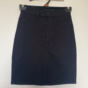 Svart jeanskjol från Gina Tricot storlek XS - Svart jeanskjol från Gina Tricot i modellen Molly. Kjolen har fejkfickor framtill, 2 bakfickor, bälteshällor och knapp- samt dragkedjestängning. Snygg, rak passform som slutar ovanför knäet. Perfekt till sneakers eller boots.