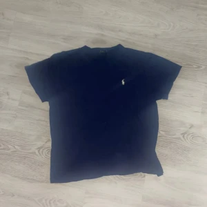 Mörkblå t-shirt från Polo Ralph Lauren - Snygg mörkblå t-shirt från Polo Ralph Lauren med klassisk passform och broderad logga på bröstet. Tillverkad i mjuk bomull och har rund halsringning samt korta ärmar. Perfekt för en clean och stilren look. Kan vara lite stor i formen 