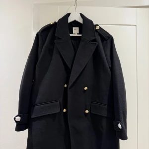 Svart rock med guldknappar från ONLY - Stilren svart rock från ONLY med markerade axlar, dubbelknäppning med guldiga knappar och snygga detaljer på ärmsluten. Klassisk krage och två stora fickor framtill. Perfekt för dig som vill ha en tidlös och cool look i höst och vinter. Slutsåld överallt! Nypris 899kr ❤️