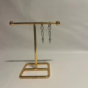 Silvriga örhängen med kedjor och spikes - Säljer ett par coola silvriga örhängen med kedjor och spetsiga spikes som hänger ner. Perfekt för dig som gillar edgy och unik stil. Örhängena har en minimalistisk design med metallkedjor och konformade detaljer.