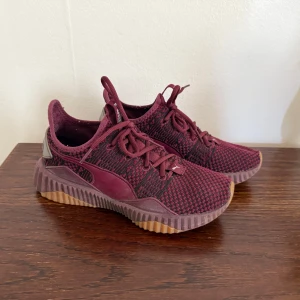  Puma - Snygga vinröda sneakers från Puma med stickad ovandel och coolt mönster. Skorna har snörning, gummisula i kontrasterande färg och silverdetaljer vid hälen. Perfekta för dig som vill ha en sportig och trendig look.