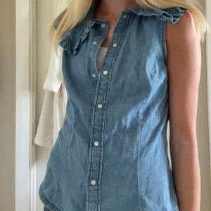 Ärmlös jeansskjorta med volangkrage - Snygg ärmlös skjorta i ljusblå jeans med volangdetaljer vid kragen. Passar super bra att styla med en T-shirt under, se sista bilden
