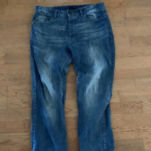 Blå jeans med tvättad look - Säljer ett par blå jeans med cool tvättad effekt och klassisk femficksdesign. Jeansen har rak passform och normal midja, vilket ger en avslappnad vibe. Materialet är slitstarkt denim och färgen är en snygg mellanblå ton med ljusare partier framtill och baktill.