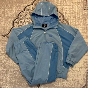 Ljusblå tracksuit 🩵 - Säljer en ljusblå träningset från FSBN med huva och dragkedja. Jackan har vita detaljer längs ärmarna och sidorna, samt elastiska muddar vid ärmslut och nederkant. Perfekt för en sportig look!🩵 Byxorna är Storlek XS och Jackan är S men byxorna blir som ett S eftersom den är baggy. Priset är inte i hugget, kan diskutera 
