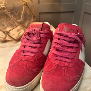 Valentino flycrews - Snygga mörk rosa och vita sneakers från Valentino Garavani med coola nitar på sulan. Ovandel i röd mocka och vitt skinn, klassisk snörning och rund tå. Knappt använda och köpa här på Plick skorna är super bra skick pris går att diskutera