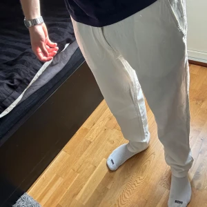 Vita linnebyxor från Selected Homme - Snygga vita linnebyxor från Selected Homme med avslappnad passform. Byxorna har dragsko i midjan, knappstängning och sidfickor. Perfekta för en chill och stilren look under varmare dagar.