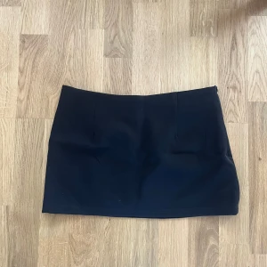 Svart kortkjol från Dazy, storlek S - Stilren svart kortkjol från Dazy i storlek S. Kjolen har en rak och tight passform med slät yta och diskret dragkedja i sidan. Insidan är fodrad för extra komfort. Perfekt för dig som gillar minimalistisk och clean stil.