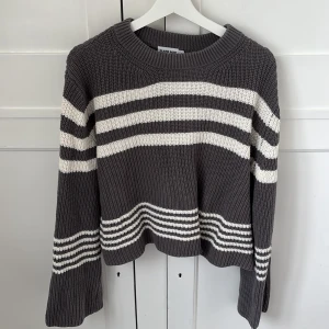 Randig stickad tröja Claire Rose - Mysig stickad tröja från Claire Rose x NA-KD i mörkgrått med vita ränder. Tröjan har en relaxed fit, rund halsringning och långa ärmar. Perfekt för lager-på-lager och chill vibes. Snyggt ribbstickad och passar till jeans eller kjol.