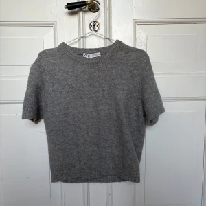 Grå stickad tröja från Zara - Mjuk och enkel grå stickad tröja från Zara i storlek M (dock lite i storleken!). Tröjan har korta ärmar, rund hals och ribbade muddar vid ärmslut och nederkant. Perfekt för lager-på-lager och chill stil. Materialet är stickat och känns skönt mot huden.💕💖