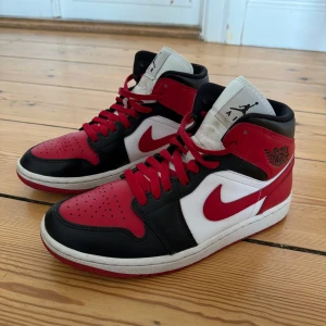 Nike Air Jordan 1 High röd/svart/vit - Säljer ett par Nike Air Jordan 1 High sneakers i klassisk Chicago-färg med röd, svart och vit skinnpanel. Snyggt högt skaft, perforerad tå och ikonisk Jordan-logga på sidan. Röd yttersula och snörning. Perfekt för dig som vill sticka ut med en ikonisk sneaker.