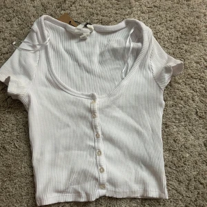 Vit ribbad croppad topp med knappar - Superfin vit croppad topp från h&m med ribbad struktur och korta ärmar.