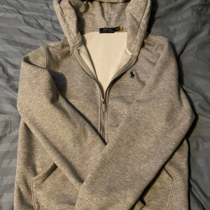 Grå hoodie från Polo Ralph Lauren - Säljer en grå hoodie från Polo Ralph Lauren med dragkedja och huva. Tröjan har lång ärm, fickor framtill och den klassiska broderade loggan på bröstet. Mjuk insida och stilren look som funkar till jeans eller joggers. Storlek M men skulle mer säga att den passar folk med stl S