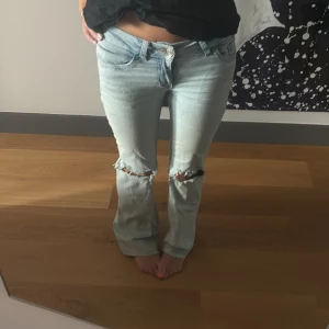 Ljusblå bootcut jeans med slitna knän - Säljer ett par ljusblå jeans med bootcut passform och slitna hål över knäna. Jeansen har klassisk femficksdesign och snygg broderad detalj på bakfickorna. Perfekta för dig som gillar en avslappnad och trendig look. Är lite ojämt klippan nertill men inget som syns, också några få fläckar, svaga, där av priset. 