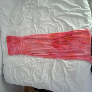 Rosa blommig långkjol från newyorker - Säljer en klänning från newyorker storlek S. Klänningen är rosa med blommigt mönster i orange och rött, har en tight passform och är gjord i ett stretchigt syntetmaterial. Köpt för 400