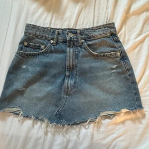 Blå jeanskjol med fransad kant från Zara - Säljer en blå jeanskjol från Zara i storlek XS. Kjolen har klassisk femficksdesign, fransad och rå kant nedtill samt slitna detaljer framtill. 