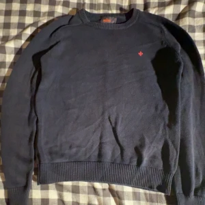 Mörkblå tröja från Morris - Mörkblå rundhalsad tröja från Morris med diskret orange logga broderad på bröstet. Tillverkad i 100% bomull och har ribbade muddar vid ärmslut och nederkant. Perfekt för dig som gillar stilren och klassisk look.