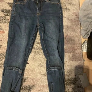 Blå cargopants i jeansmaterial - Säljer ett par blå cargopants i jeansmaterial med klassiska fickor på benen och bakfickor. Byxorna har en rak passform och normal midja, perfekta för dig som gillar en avslappnad streetstil. Snygga detaljer med sömmar och slitningar som ger en cool vibe.