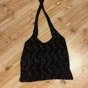 Svart glittrig halterneck topp - Snygg svart halterneck med glittrigt vågmönster. Är i storlek M men passar även en Xs/S