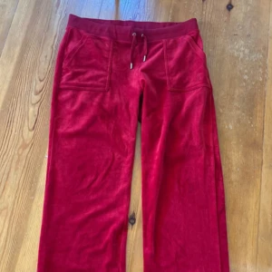 Röda velourbyxor Juicy Couture L - Mysiga röda mjukisbyxor från Juicy Couture i velour med bred resår och snörning i midjan. Byxorna har raka ben, stora fickor fram och broderad JC-logga på ena fickan. Perfekta för chill eller streetstyle.
