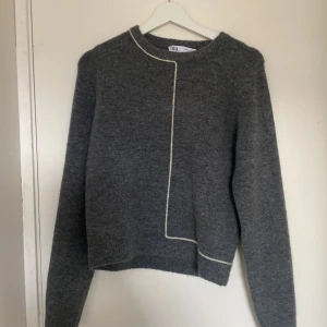 Grå stickad tröja från Zara - Mysig grå stickad tröja från Zara med lång ärm och rund hals. Tröjan har en unik vit kontrastsöm som går längs framsidan och baksidan. Perfekt för lager-på-lager och chill höst- och vinterstil. Tröjan är i medium men är lite liten i storlek och passar även S/XS