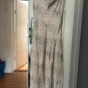 Beige långklänning med svarta prickar - Säljer en snygg långklänning från Gina Tricot i beige med svarta prickar. Klänningen har tunna axelband och en mjukt draperad halsringning. Materialet är glansigt och känns lyxigt mot huden, perfekt för dig som gillar trendiga mönster och stilren look💕 använd fåtal gånger. Klänningen har även en slits på sidan🌸