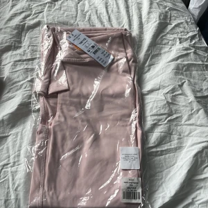 Ljusrosa sportig kjol i syntet - Säljer en ljusrosa, sportig yoga pants i mjukt syntetmaterial. Byxorna har en enkel och clean design med smala sömmar och stretchig passform, perfekt för dig som gillar att röra på dig. Passar dig som vill ha en bekväm och snygg look.