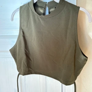 Olivgrön croppad linnetopp  - Snygg olivgrön croppad linnetopp från SHEIN och smala knytband som kan lindas runt midjan. Toppen är ärmlös och har en enkel knappstängning i nacken. Perfekt för dig som gillar trendiga och stilrena plagg.