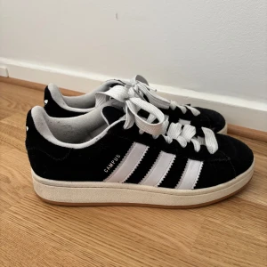Svarta Adidas Campus sneakers - Obs: ligger uppe till försäljning på andra sidor också så skriv gärna innan ni köper.                   Säljer mina fina älskade Adidas Campus skor. De är svarta och vita. De är något använda men jag tycker inte man ser mer än några små små slitningar på tyget. Jag har försökt göra rent de så gott de går, och vill ni att jag tvättar snörena först så gör jag sjävklart det! 🙏🏼🖤☺️ normala i storleken! Säljer för lite mindre än halva!  Inköpspris: 1345kr