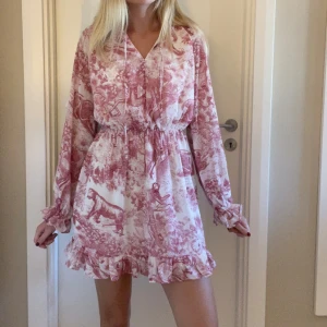 Vit och rosa kortklänning med volang - Supersöt kortklänning i vitt och rosa med unikt mönster och volangkant. 