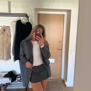 Grått set från Pull&Bear - Säljer ett stilrent grått set från Pull&Bear. Setet består av en ”jacka” med dragkedja och fickor samt en matchande minikjol. Cargofickor på. Perfekt för dig som vill ha en modern och snygg look. Storlek M i kjolen och S i ”jackan”. Så snyggt!!