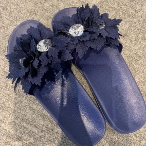 Mörkblå tofflor - Säljer ett par mörkblå sandaler med stora dekorativa blommor och glittrande strassdetaljer ovanpå. Skorna har platt sula och är perfekta för att sticka ut med en unik stil. Superfina till sommaren! 
