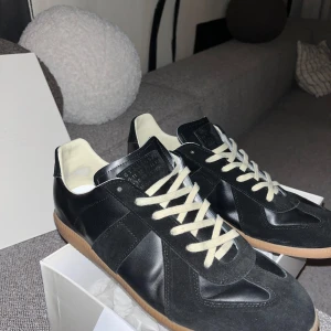 Maison Margiela Gats - Säljer ett par svarta Maison Margiela Gats sneakers med beige snörning och gummisula. Storlek 45. OG fås med.
