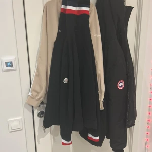 Svart Moncler jacka med röd, vit och blå detalj - Säljer en svart jacka från Moncler med snygga ribbade muddar i rött, vitt och blått. Jackan har dragkedja och klassisk Moncler-logga på bröstet. Perfekt för dig som vill ha en stilren och sportig look. 