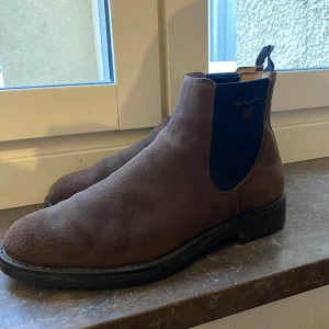 Bruna chelsea boots från Gant - Säljer ett par bruna chelsea boots från Gant i mocka. Jag har aldrig använt dom och killen jag köpte dom av har knappt de heller. I väldigt fint skick son man ser på bilderna.