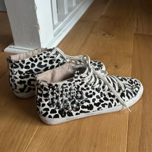 Leopardmönstrade sneakers med nitar - Säljer ett par coola sneakers med svartvitt leopardmönster och silvriga nitar på sidorna i storlek 41 men passar även 39 och 40. Skorna har snörning och dragkedja på sidan för enkel påtagning. Perfekta för dig som vill sticka ut med din stil!