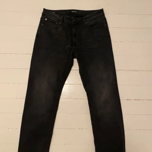 Jack & Jones jeans  - Snygga svarta jeans från Jack & Jones med en klassisk femficksdesign. De har en dragkedja och knapp framtill. Perfekta för en stilren look. Hör av dig vid frågor och funderingar!