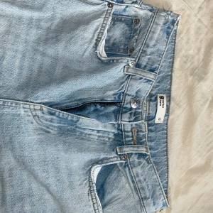 Ljusblå slitna jeans med hål - Säljer ett par ljusblå jeans från Gina Tricot med stora slitningar på båda knäna. Jeansen har normal passform, klassisk femficksdesign och dragkedja i gylfen. 