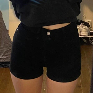 Svarta jeansshorts från Gina Tricot Molly - Svarta stretchiga jeansshorts från Gina Tricot, modell Molly. Klassisk femficksdesign med uppvikta benslut och hög midja. Perfekta för sommaren och enkla att matcha med olika toppar.