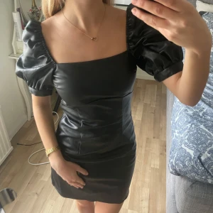 Svart kort klänning med puffärmar och snörning i ryggen - Säljer en svart kort klänning med fyrkantig urringning och puffiga kortärmar. Klänningen har snygg snörning i ryggen som ger en unik detalj. Perfekt för dig som vill sticka ut med en trendig look.