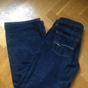Mörkblå jeansbyxor med raka ben - Säljer ett par mörkblå jeansbyxor med raka ben och klassiska fickor bak. Byxorna har kontrastsömmar och en enkel design utan extra detaljer. Perfekta för en avslappnad stil.